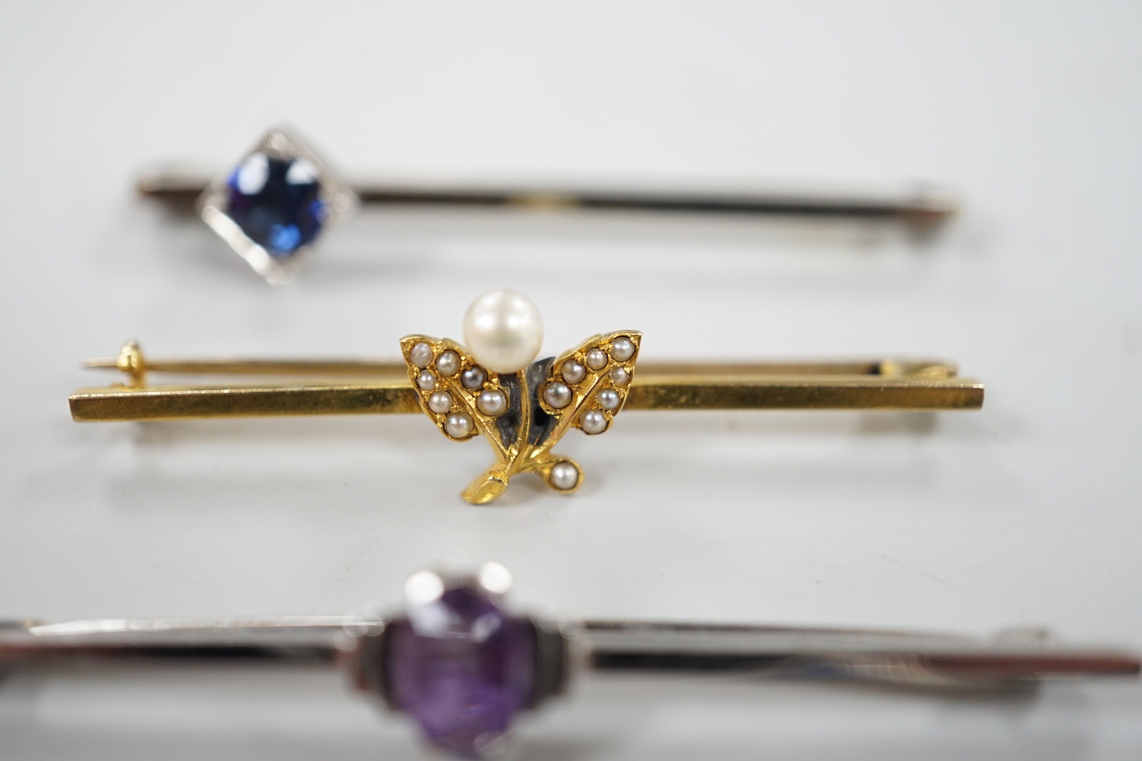 A 9ct white gold and synthetic? sapphire set bar brooch, 45mm and three other bar brooches including yellow metal and seed pearl, white metal and seed pearl and a 9ct and amethyst bar brooch, gross weight 8.1 grams.